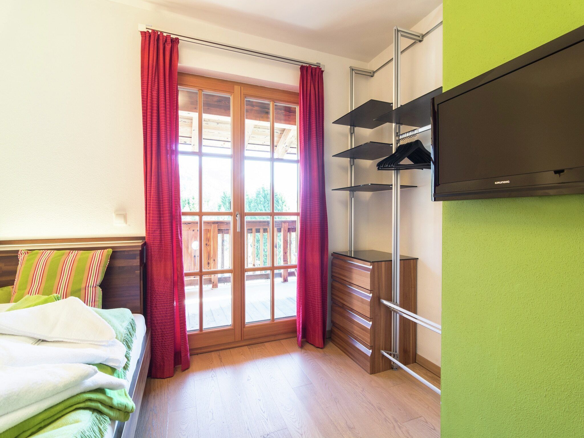 Ein Zimmer mit einem Bett, einem an der Wand befestigten Fernseher, einer Holzkommode und einer Glastür zum Außenbereich.