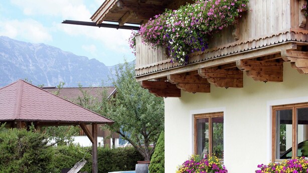 A chalet with a wooden balcony, flower boxes, a hammock, and a mountain backdrop. - Apartment in Waidring near PillerseeTal Ski Area (Waidring)