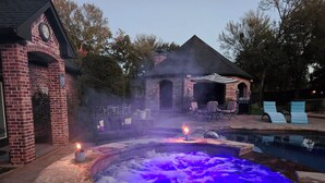 Ett bubbelbad med blått ljus, omgivet av en innergård med tegelbeläggning, utemöbler och en pool.