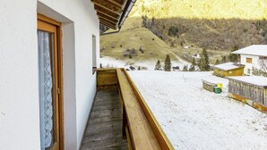 Een balkon met een houten vloer en uitzicht op een besneeuwd landschap met huizen en bomen.
