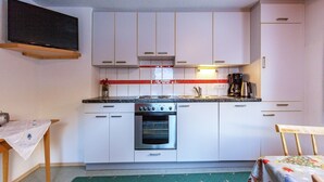 Een kleine keuken met witte kastjes, een fornuis, oven en koffiezetapparaat.