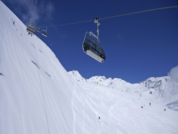 A ski lift chair suspended over a snowy slope with skiers below.