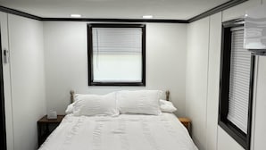 Une chambre à coucher avec un lit, une table de chevet, une fenêtre avec des stores et un luminaire au plafond.