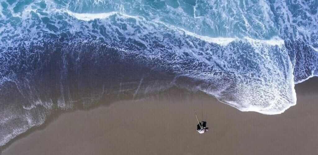 A beach with a large wave approaching a person standing on the sand.