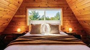 Een slaapkamer met een schuine kap, een groot raam, een bed met kussens en twee bedlampjes.