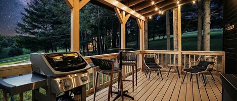 A deck with a grill, chairs, and a view of the night sky.