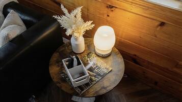 Une table ronde en bois, sur laquelle se trouvent un vase blanc, une plante décorative, un magazine et une lampe blanche.