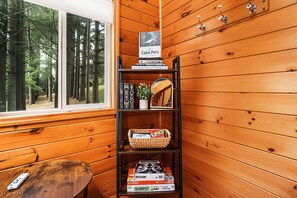A wooden bookshelf with books and a board game, a window with a forest view, and a wooden bench.