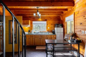 A wooden cabin interior with a kitchen, dining area, and a staircase. - Starlit Hot Tub & Fire Pit | Modern Cabin for Two (Logan)