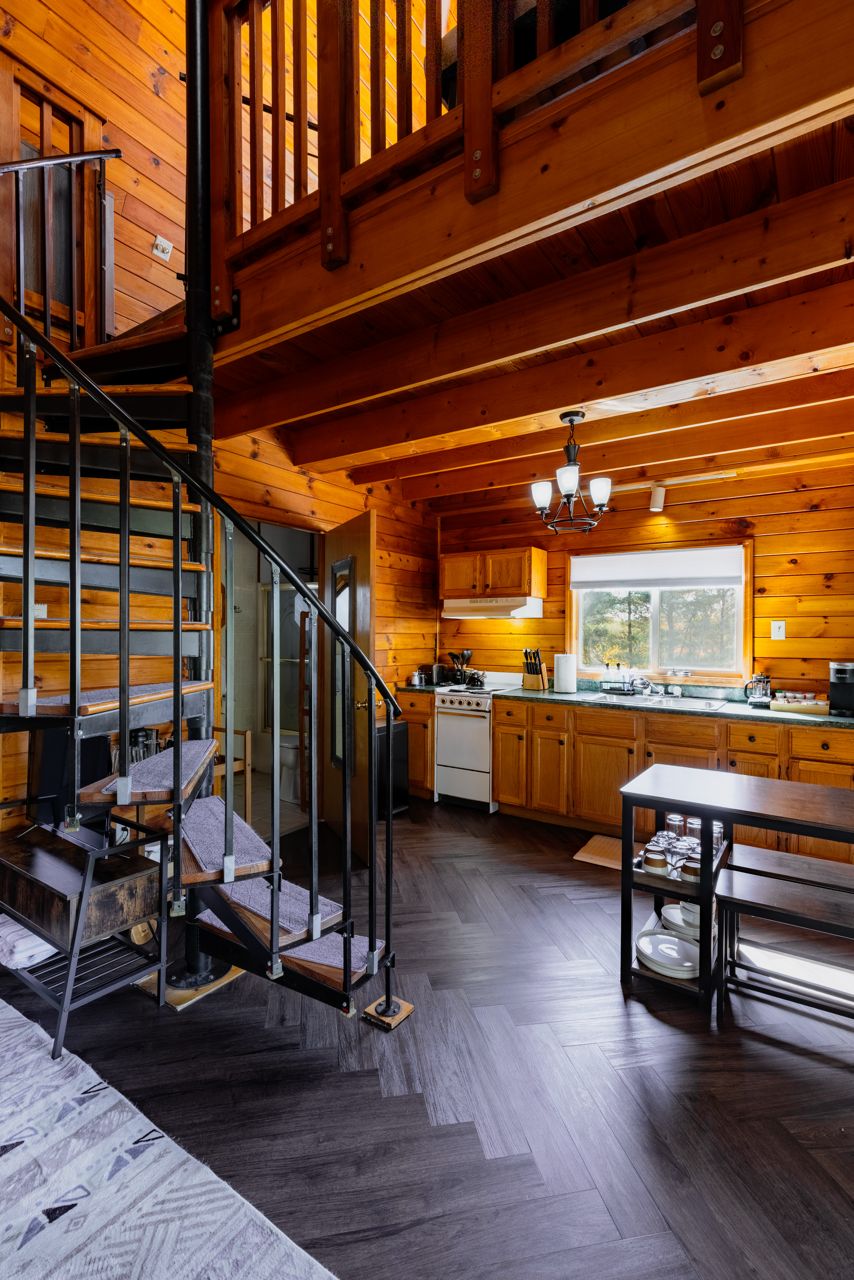 L’intérieur d’une cabane en bois, avec un escalier, une cuisine et un coin repas.