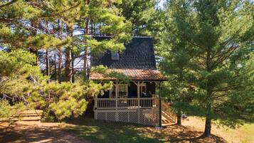 Une cabane dotée d’une véranda, entourée de pins et bordée d’un chemin de gravier.