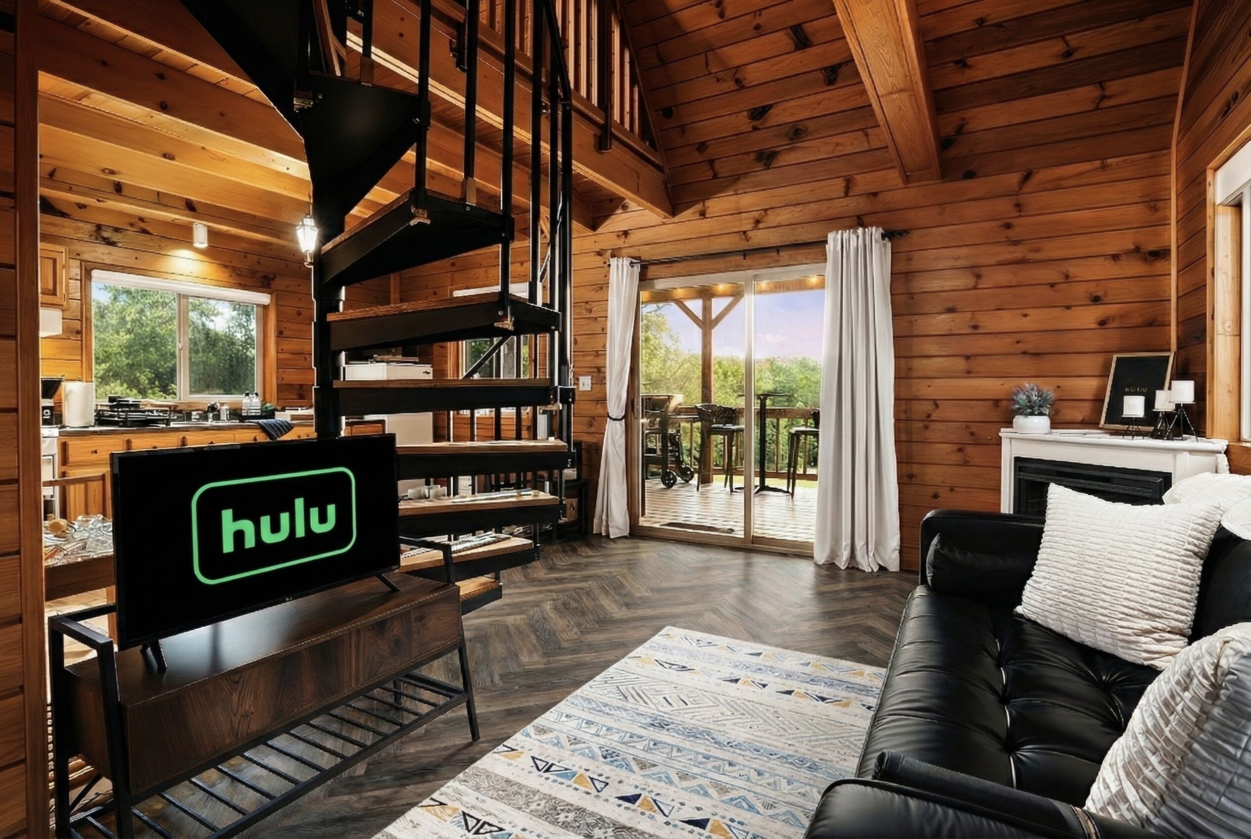 A wooden cabin interior with a living area, a fireplace, a dining area, and a large window.