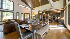 A spacious living area with a large wooden dining table, leather sofas, and a kitchen in the background. - Ring of Fire -5 Master Suites,Sleeps 24-Basketball Ct & More! (Broken Bow)