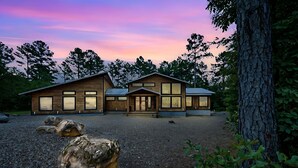 A wooden cabin with a gravel driveway and large rocks in front, surrounded by trees. - Ring of Fire -5 Master Suites,Sleeps 24-Basketball Ct & More! (Broken Bow)