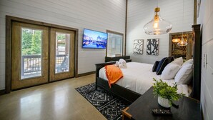 A bedroom with a large bed, a TV on the wall, and a balcony with a view. - Ring of Fire -5 Master Suites,Sleeps 24-Basketball Ct & More! (Broken Bow)