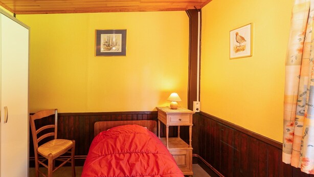 A small, cozy room with a wooden bed, a chair, a nightstand with a lamp, and two framed pictures on the wall. - Charming Chalet in Vielsalm (Vielsalm)