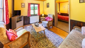 A cozy room with a wooden ceiling, a television, a sofa, a chair, a table, and a bed.