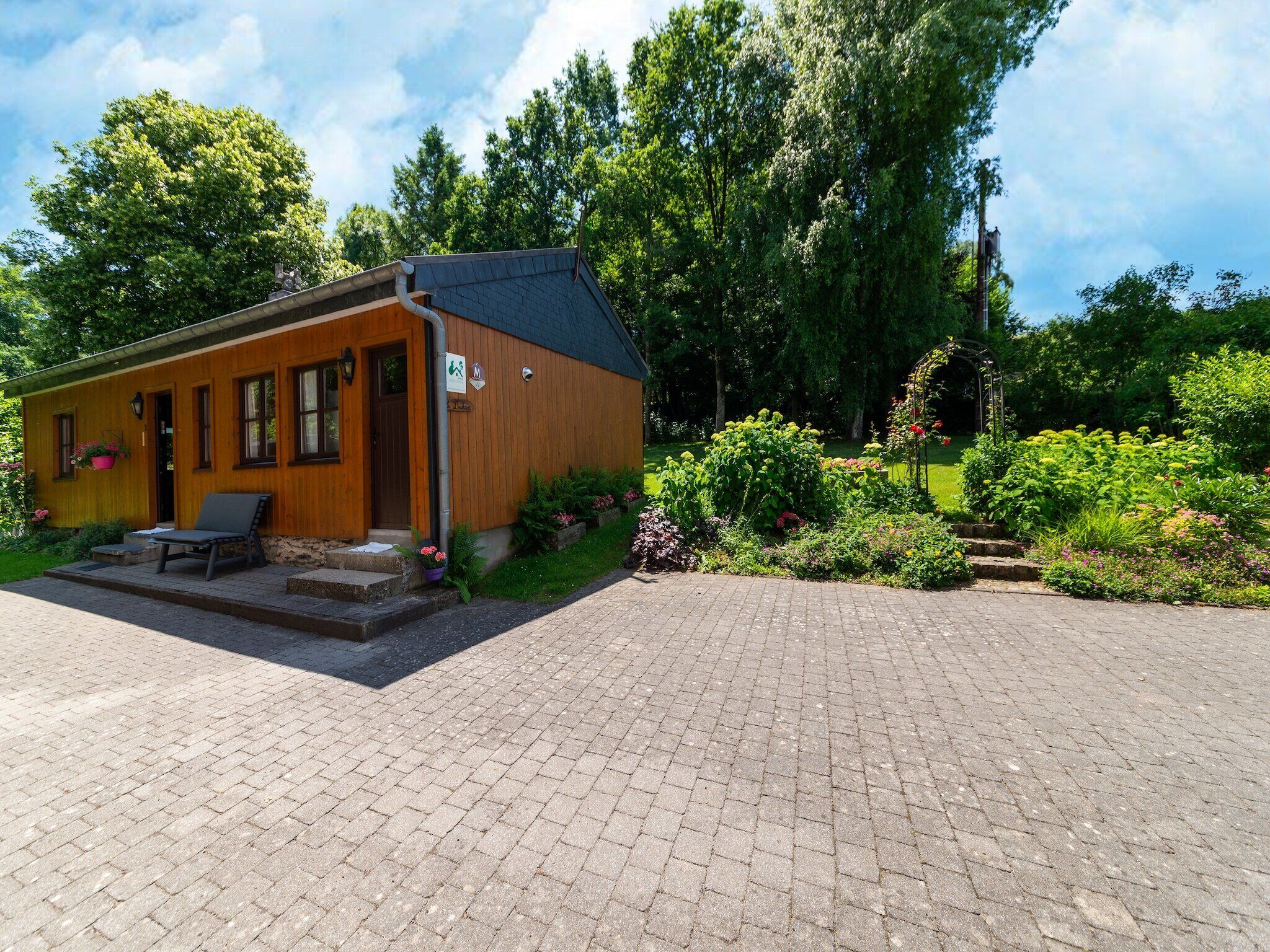 Une cabane en bois avec un porche, une chaise et un jardin où poussent différentes plantes et fleurs.