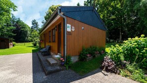 A wooden cabin with a porch, a sign indicating it is a men's restroom, and a garden area with plants and flowers.