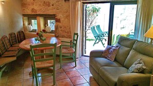 Una sala de estar acogedora con un sofá, una mesa de comedor con sillas y vistas al exterior a través de un ventanal.