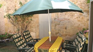 Une terrasse avec une table et des chaises, un parasol et un mur de pierre en arrière-plan.