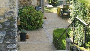 Una escalera de piedra que conduce a un patio con jardín, mobiliario exterior y una parrilla.