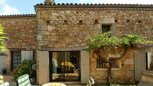 Un edificio de piedra con fachada rústica, una ventana pequeña y una puerta que da a un espacio exterior con una mesa y sillas.
