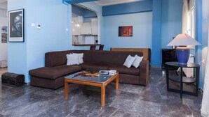 A living room with a brown sectional sofa, a wooden coffee table, and a blue lamp on a side table. - Classic Koukaki Living 2 Bd with Balcony (Athens)