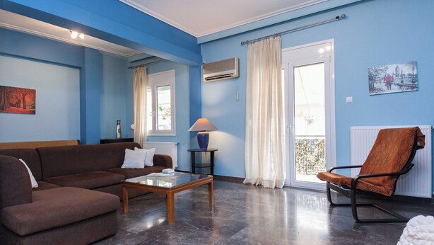 A living room with a brown sofa, a wooden coffee table, a blue vase, and a patterned orange chair. - Classic Koukaki Living 2 Bd with Balcony (Athens)