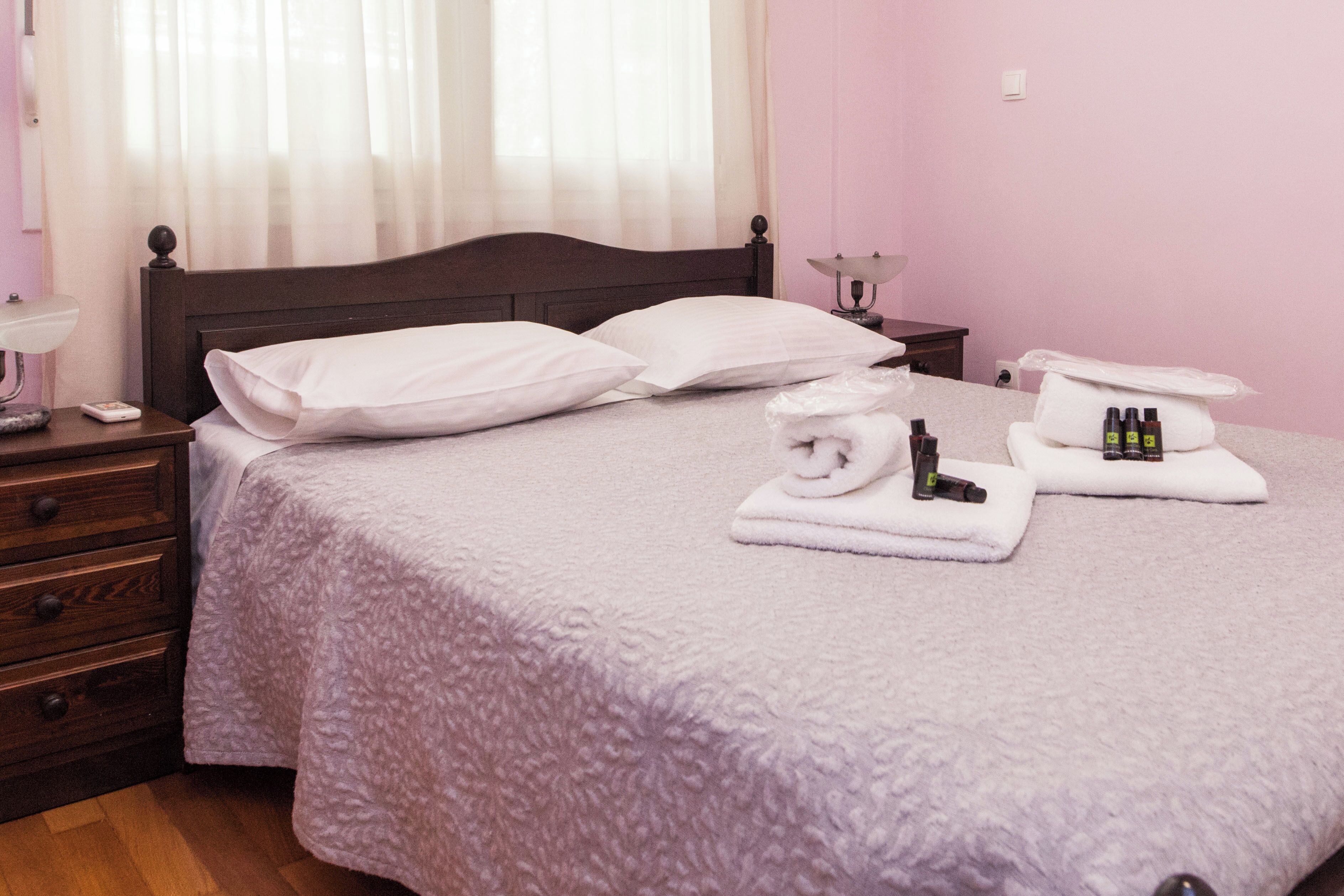 A neatly made bed with white linens, a bedside table with a lamp, and toiletries on the bed.