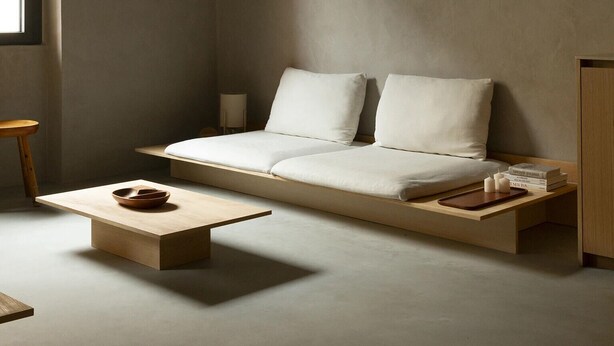 Een minimalistische woonkamer met een bank, een salontafel en een bijzettafeltje met boeken en kaarsen.