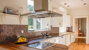 A modern kitchen with a central island, a built-in stove, and a window overlooking greenery. - A grand, newly renovated villa in a castle setting (Stora Sundby)