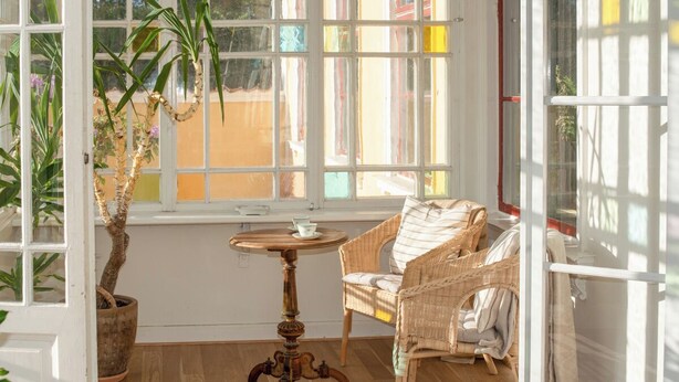 A room with a wicker chair, a small round table, and a potted plant. - A grand, newly renovated villa in a castle setting (Stora Sundby)