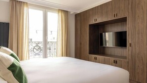 Habitación de hotel con una cama grande, televisión integrada, paneles de madera y un balcón con barandilla.