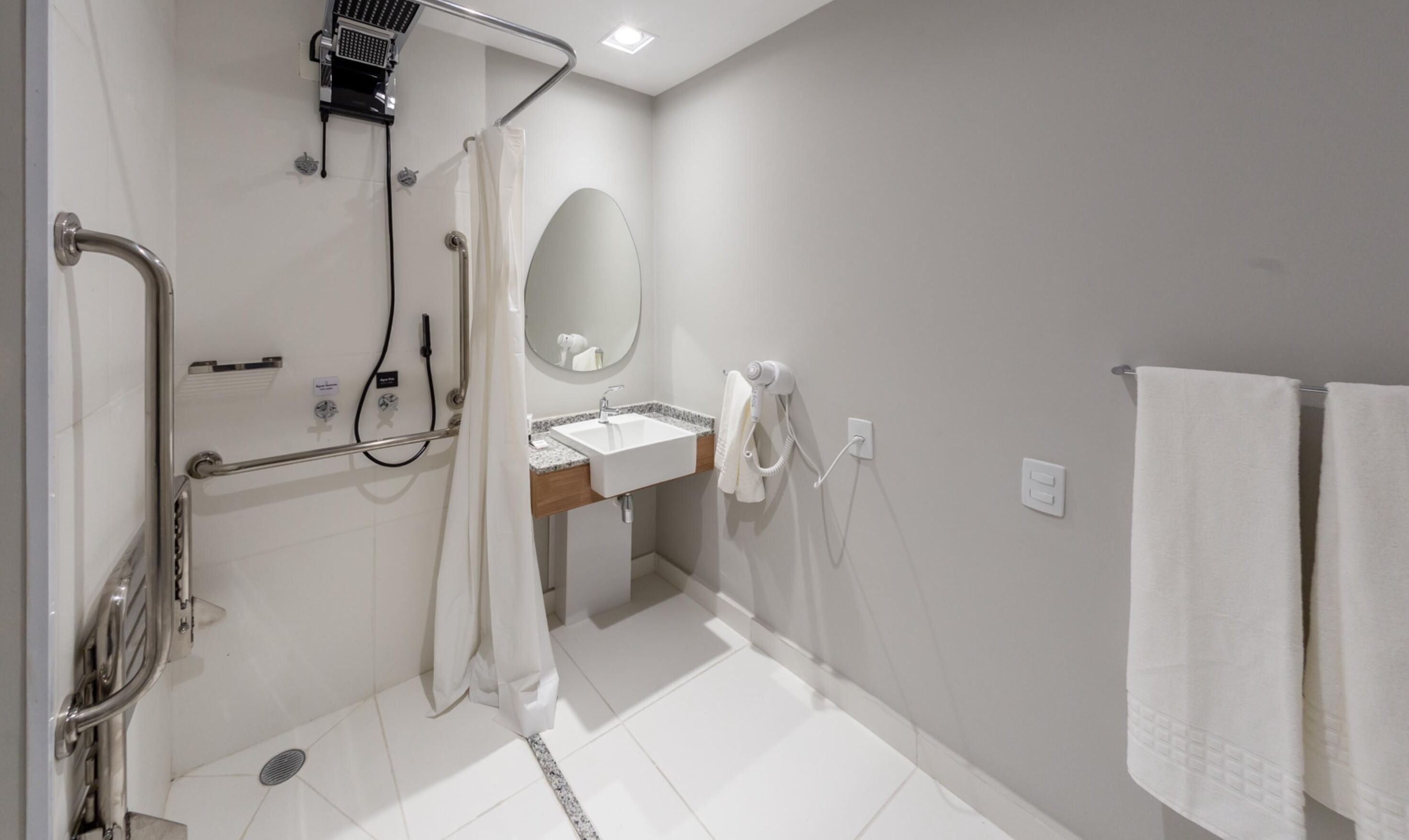 A modern bathroom with a shower, grab bars, a sink, and a mirror.