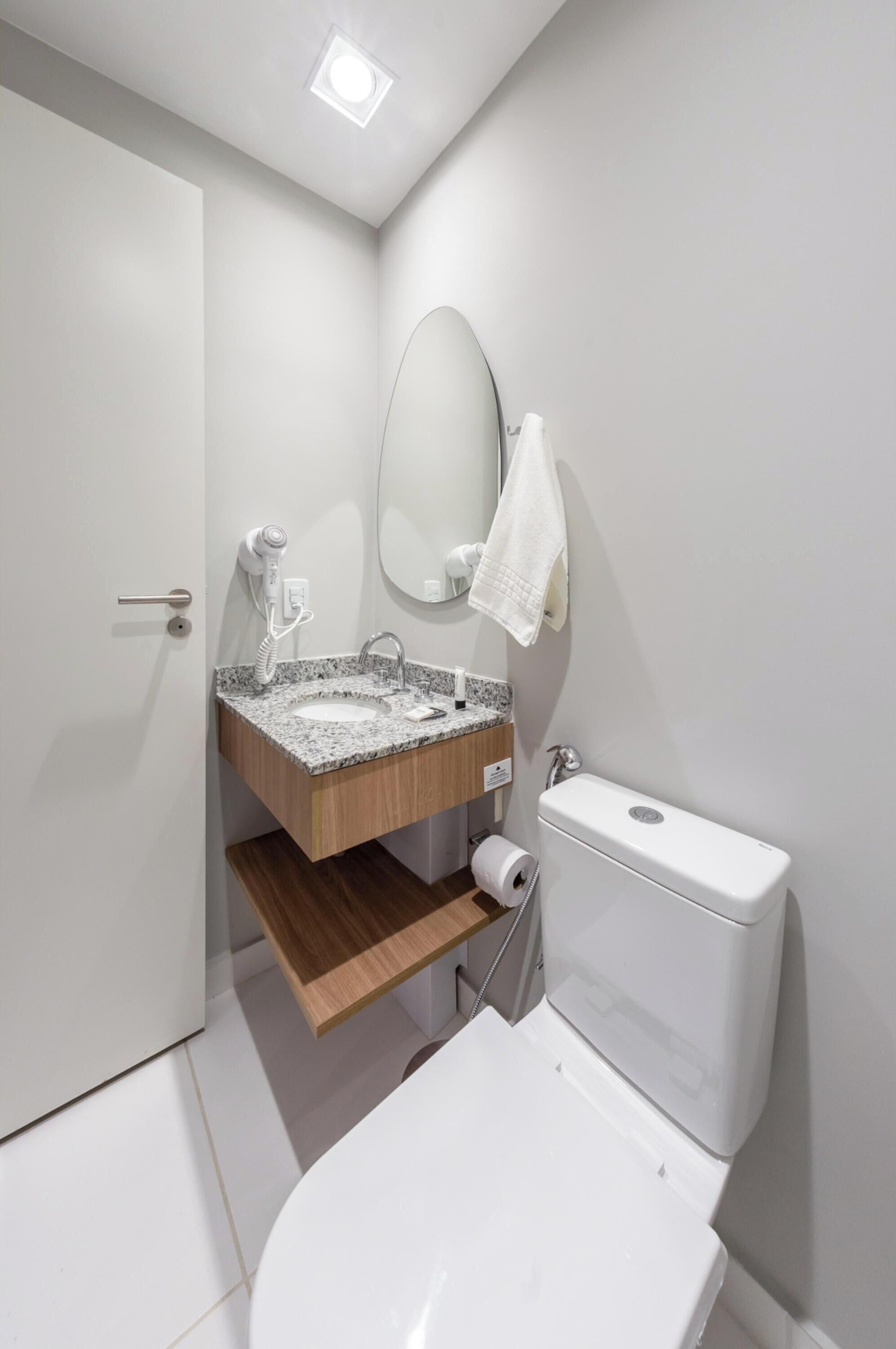 A modern bathroom with a white toilet, a granite sink, a wooden vanity, and a mirror.