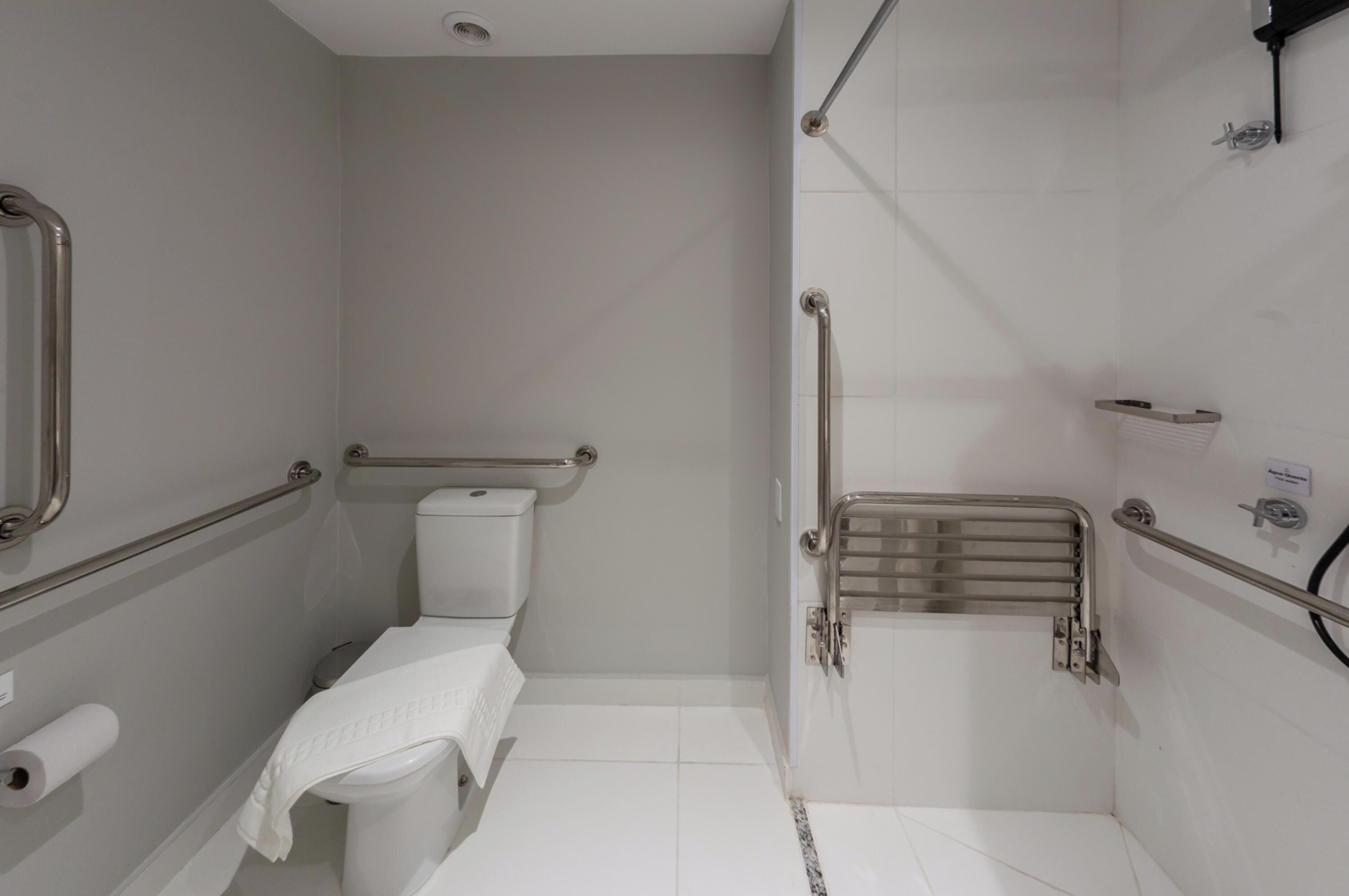 Un baño pequeño y moderno con inodoro, zona de ducha con barra de apoyo y un perchero para toallas.