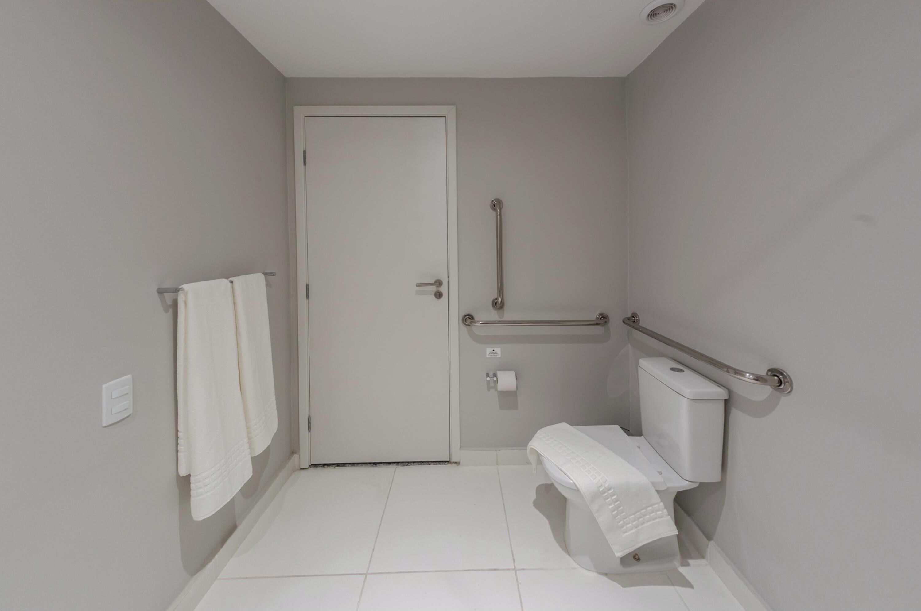 Une petite salle de bain propre, équipée de toilettes, d’une barre d’appui et d’un porte-serviettes.