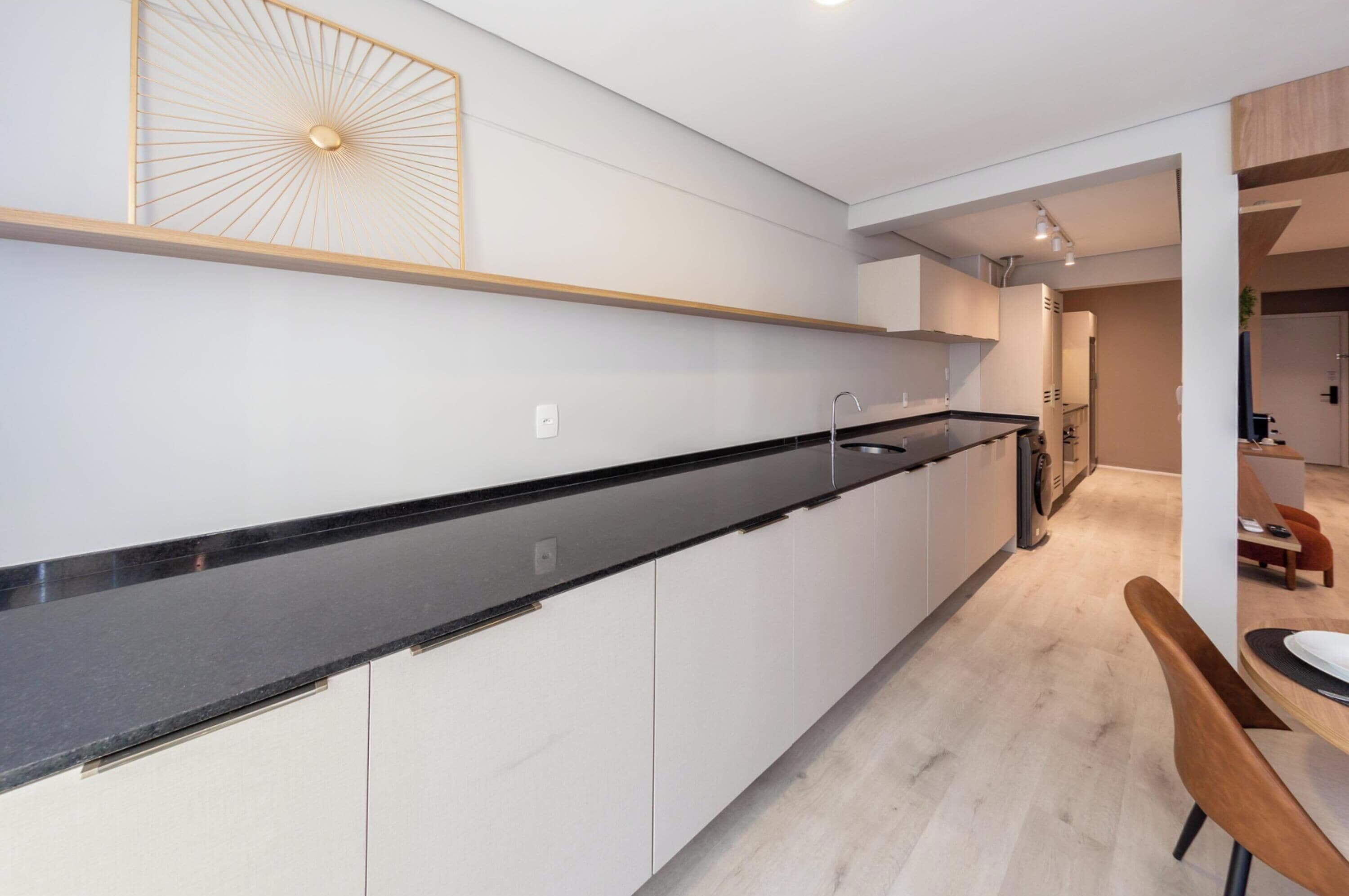Eine moderne Küche mit schwarzem Arbeitsplatz, weißen Schränken und einem Essbereich mit Holztisch und Stühlen.