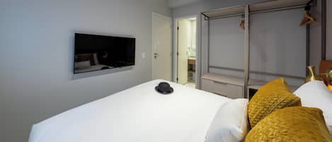 Hotellihuone, jossa on sänky, seinälle asennettu televisio, vaatekaappi ja ilmastointilaite.
