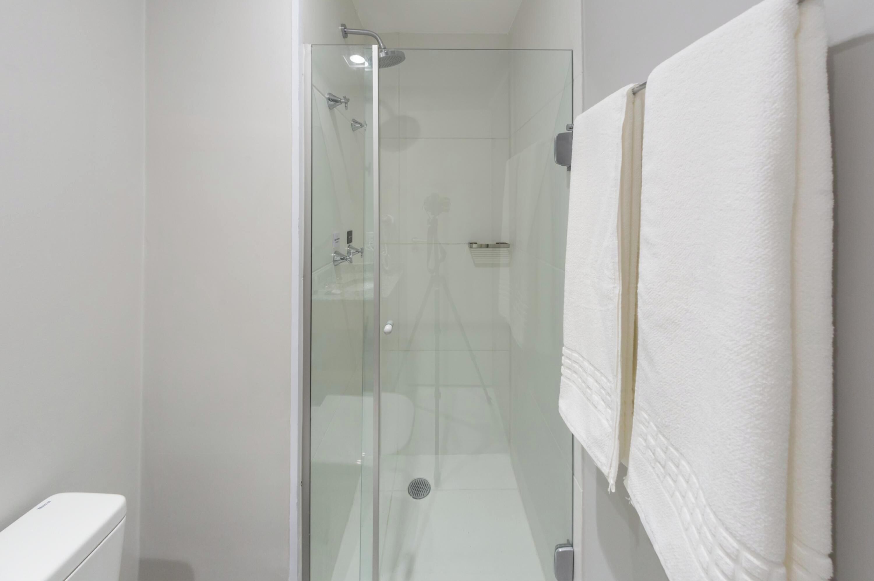 A glass-enclosed shower stall with a white towel hanging on the wall.