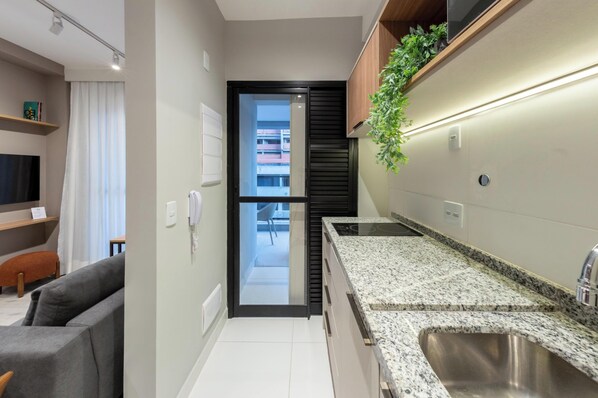 Une cuisine moderne dotée de plans de travail en granit, d’un évier en acier inoxydable et d’une porte coulissante à cadre noir donnant sur un balcon.