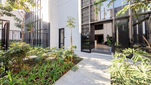 Un bâtiment moderne doté de grandes fenêtres, d’une cour intérieure agrémentée de plantes et d’un chemin menant à l’entrée.