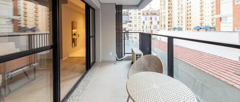 Un balcón con una zona de estar, una puerta de vidrio que da a una habitación y vistas de edificios cercanos.