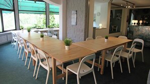 A conference room with a long wooden table, white chairs, and potted plants.