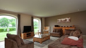 A spacious living room with a large television, comfortable seating, and a view of a garden through large windows. - Peer Villa with Garden (Peer)