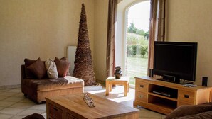 A living room with a sofa, a coffee table, a television on a wooden stand, and a tall, textured plant. - Peer Villa with Garden (Peer)