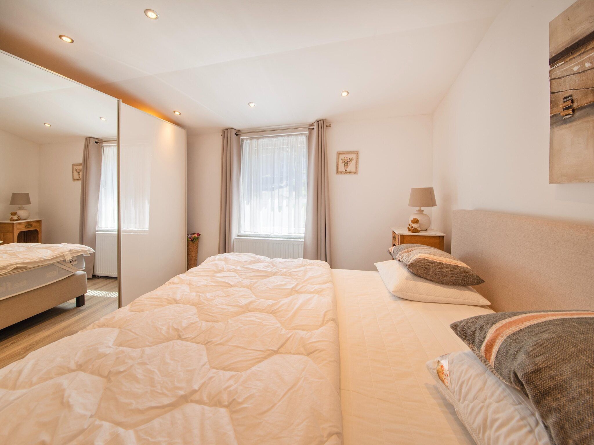Une chambre à coucher avec un grand lit, une table de chevet avec une lampe, un miroir et une fenêtre avec des rideaux.