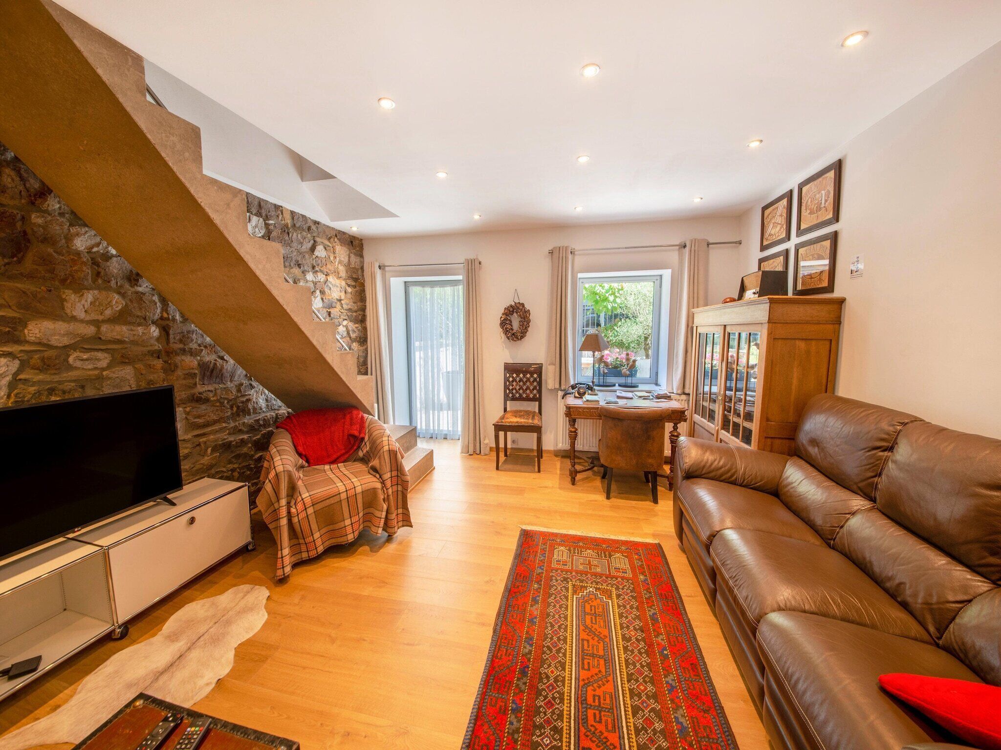 A living room with a stone wall, a TV, a sofa, a desk, and a window with curtains.