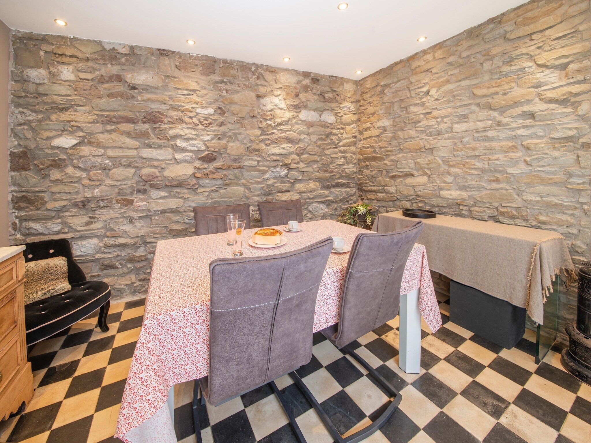 Un comedor de paredes de piedra con suelo a cuadros, una mesa dispuesta con un pastel y sillas.